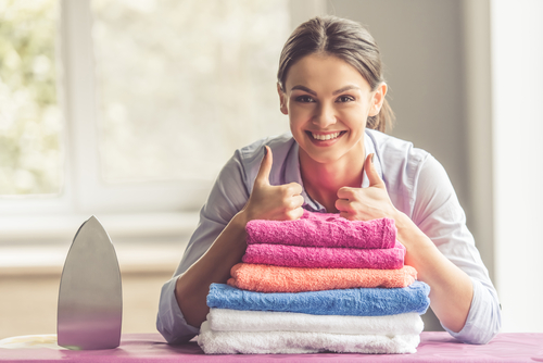 beautiful-young-woman-is-leaning-on-ironing-board-showing-ok-sign-looking-at-camera-and-smiling